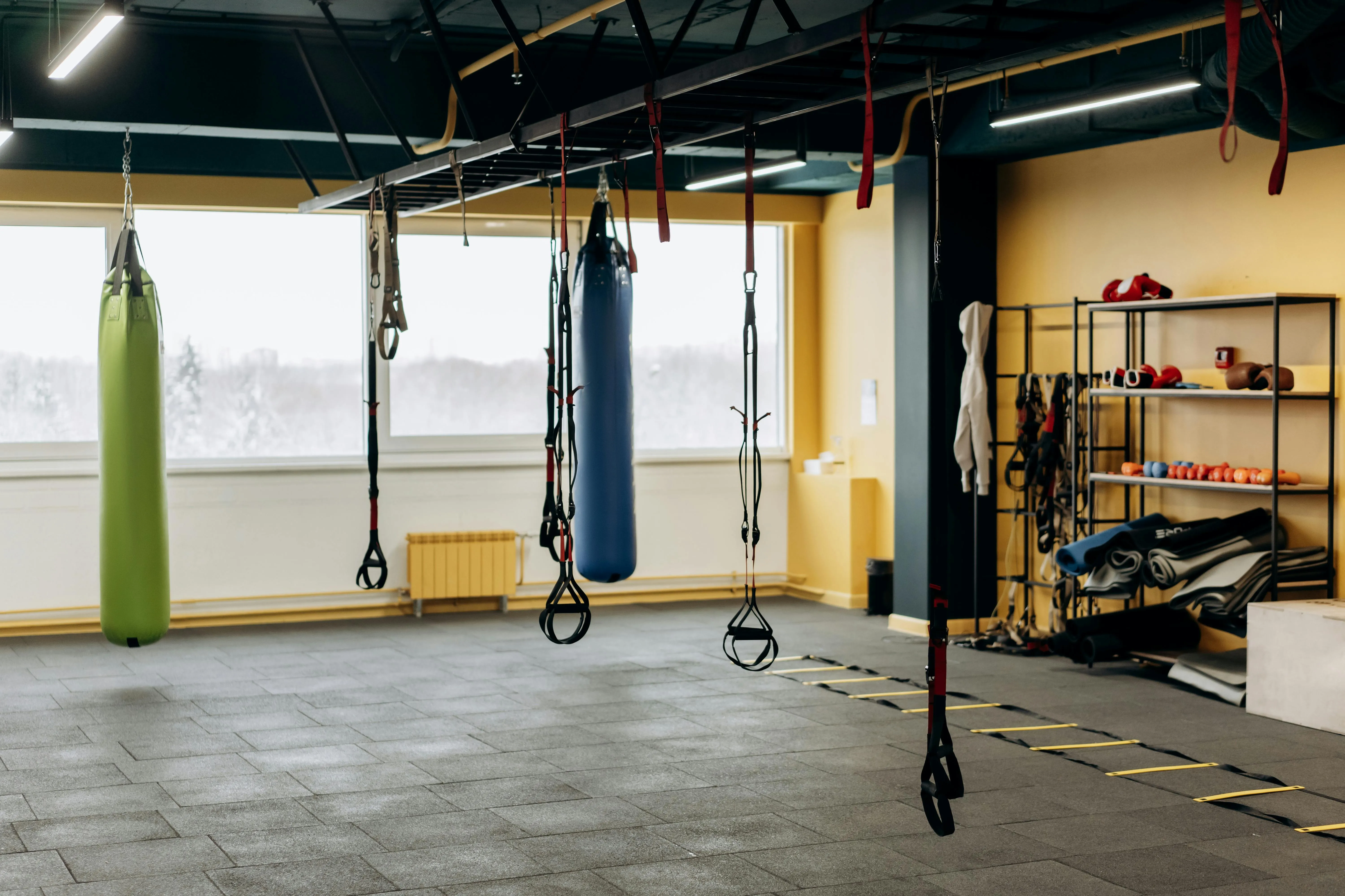 There are two punching bags, one lime-colored and the other bright blue, in a large gym along with other tools and equipment. 