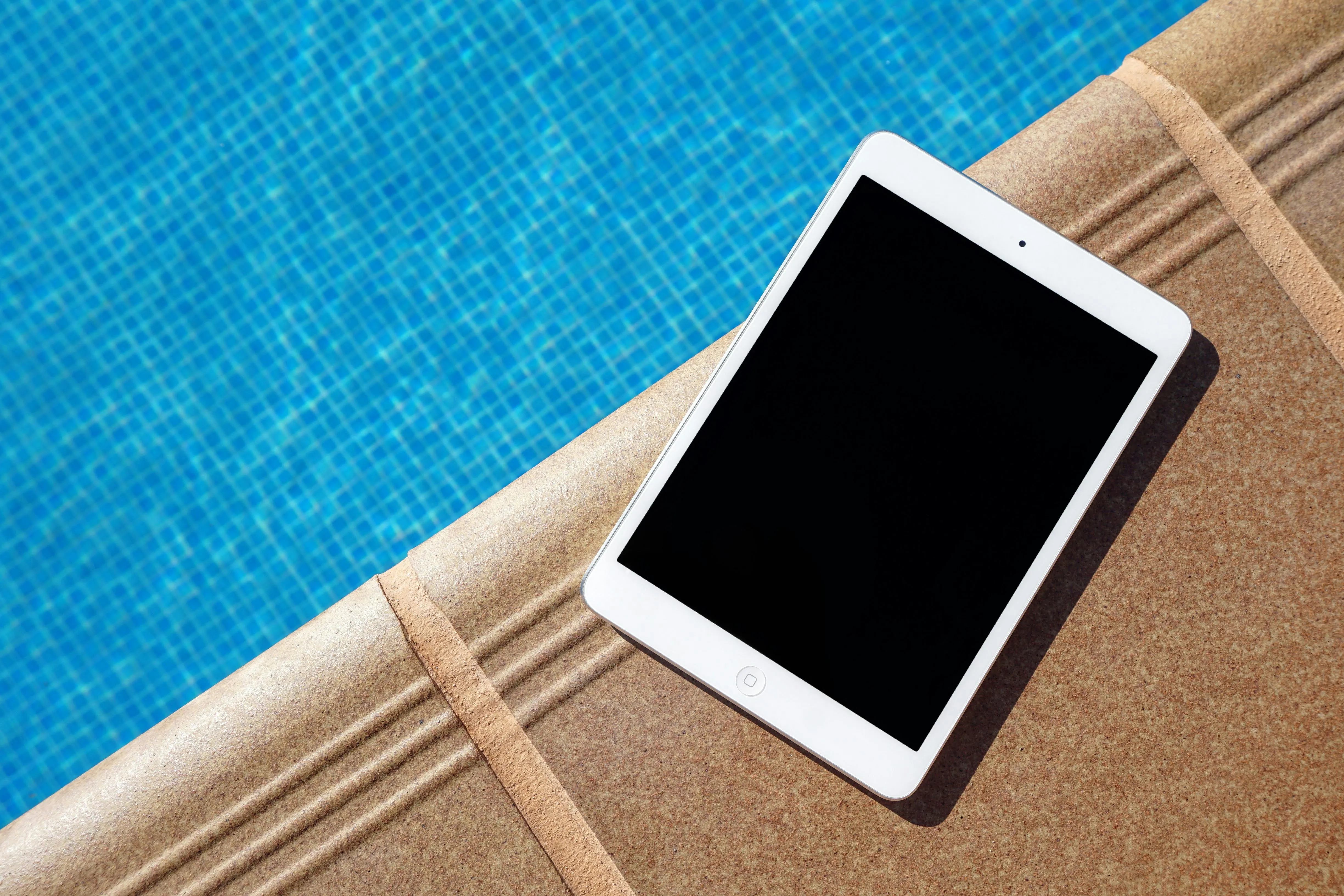 An ipad near a pool on a brown surface.