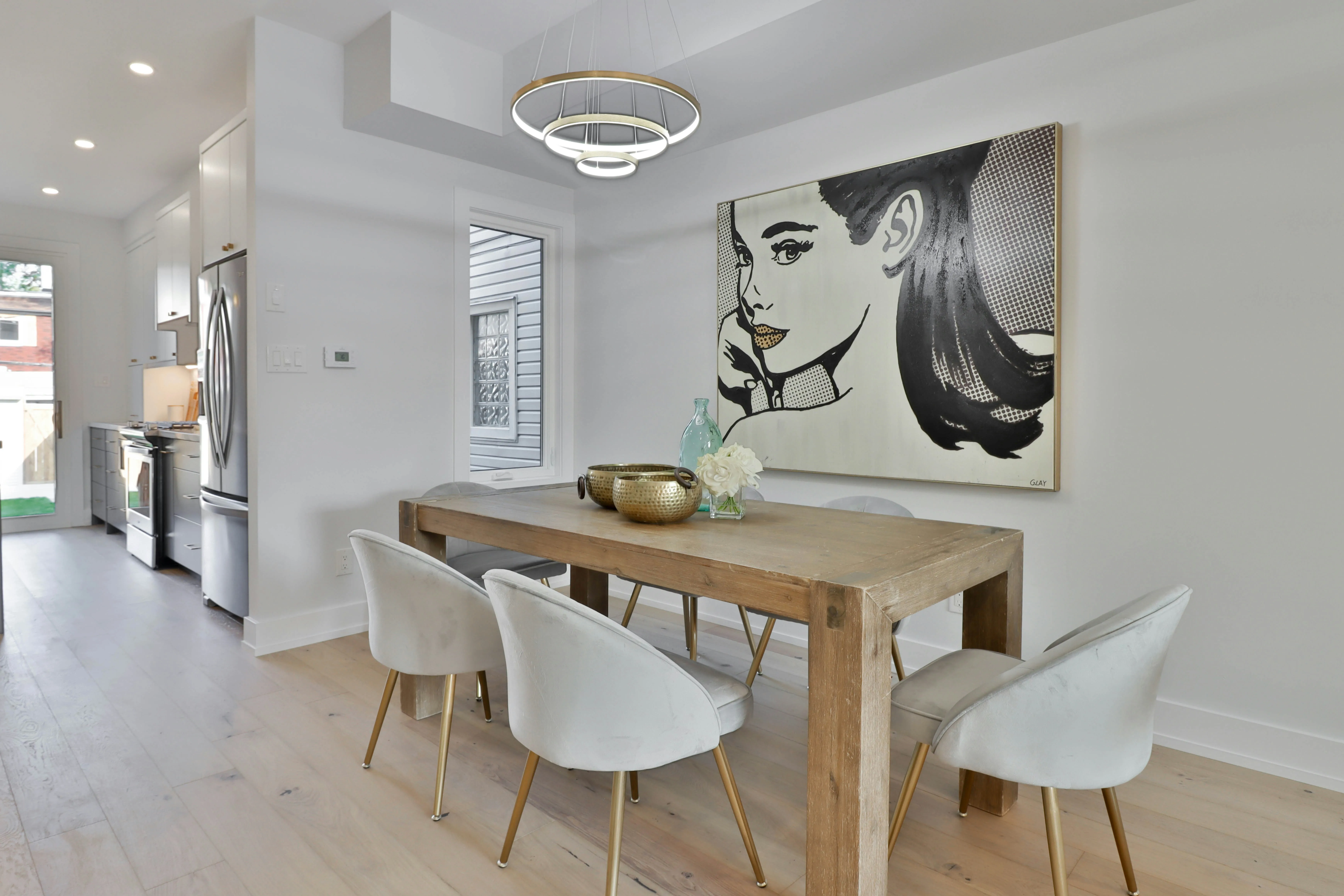 A brown wooden dining table with white chairs. On the wall of the dining room there is a huge wall art.