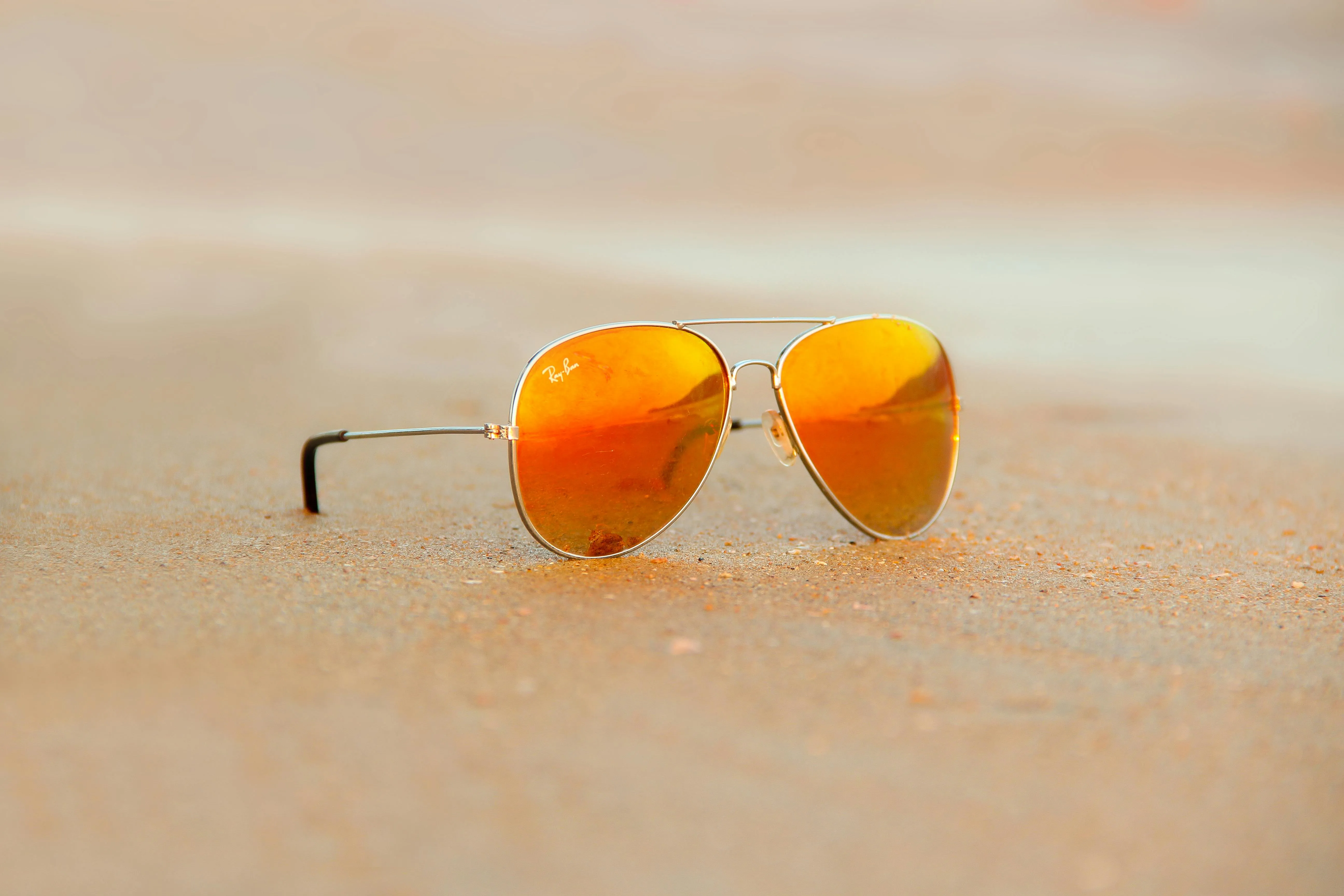 A pair of orange tinted aviator sunglass on sandy beach.