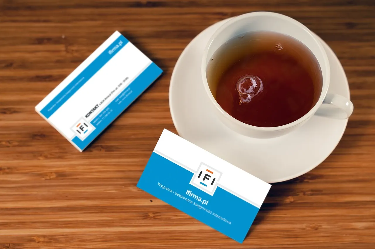 Two business cards on a wooden surface along with a cup of tea.