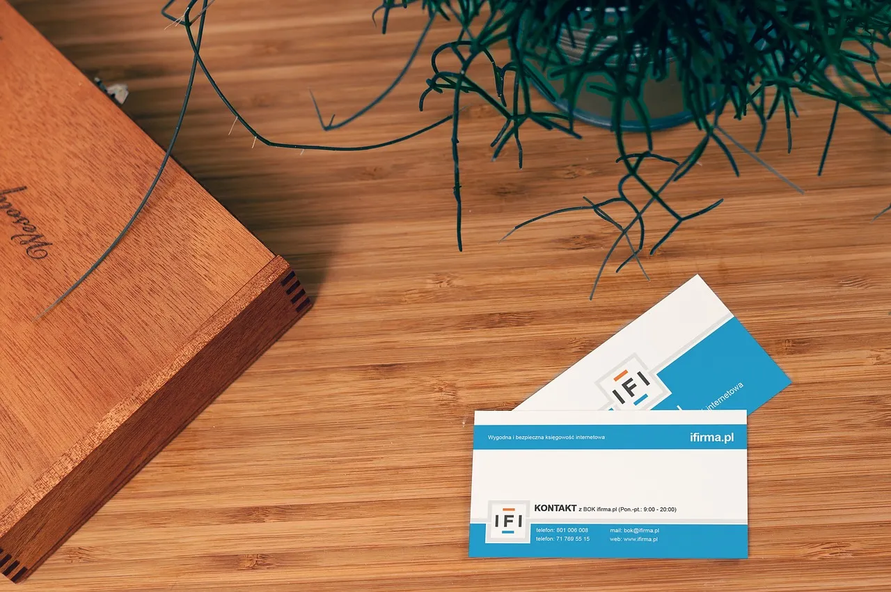 Two business cards on a wooden table. Near them is some artifical grass and a box.