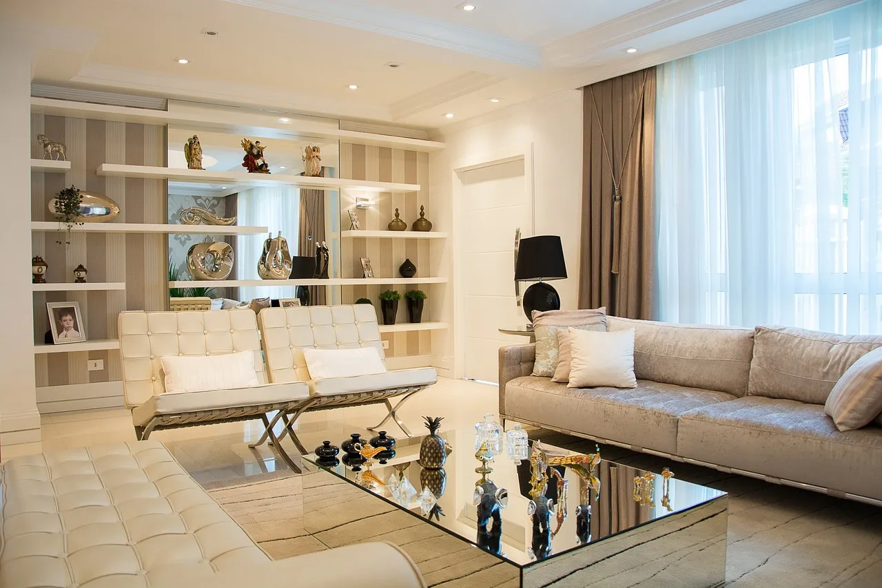 A stylish living room featuring furniture that looks modern, like a sofa and two chic accent chairs. Between the seats, there is a table. A cabinet that houses numerous decorative items can also be seen in the room.