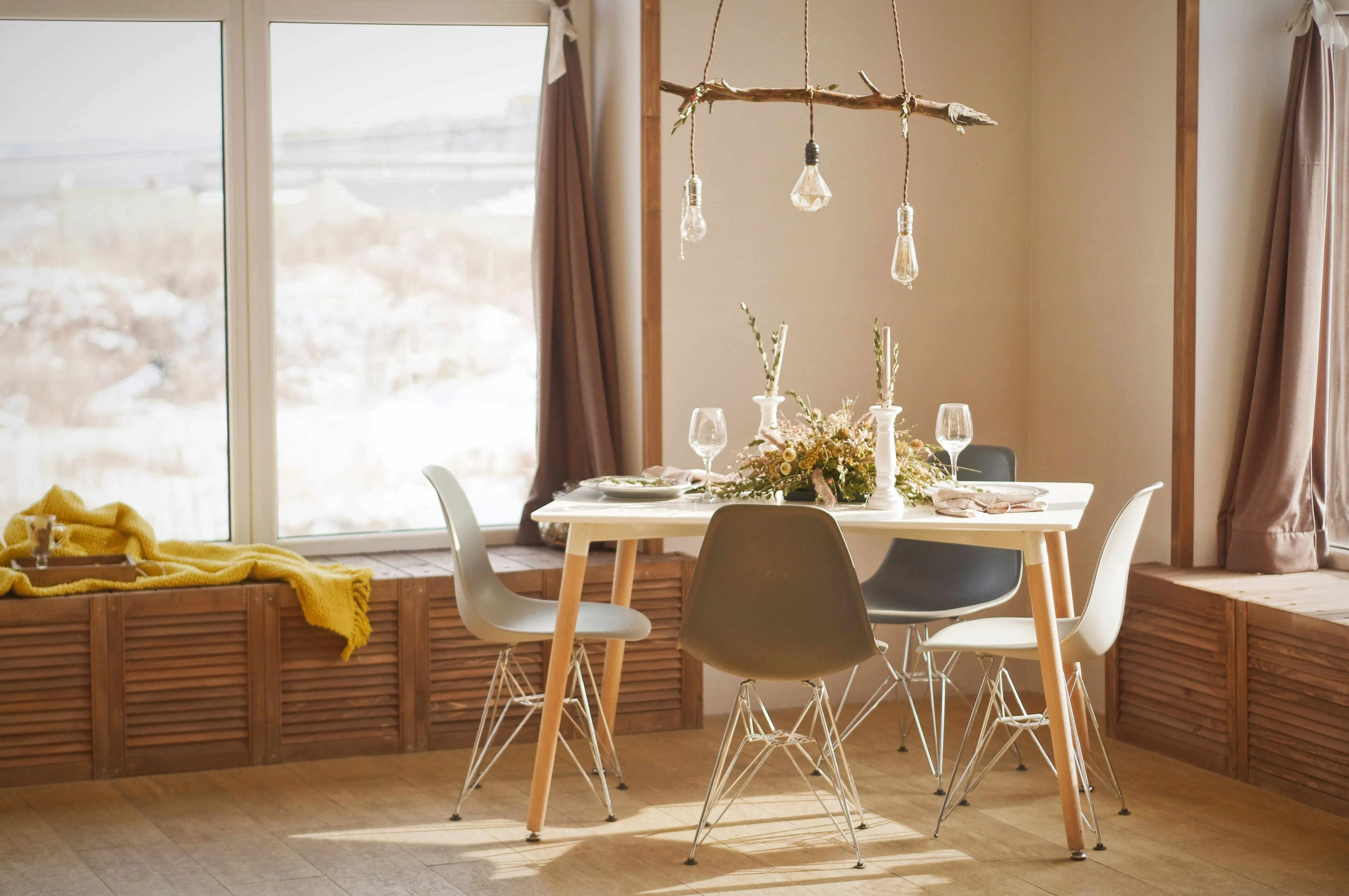 White wooden dining table set near a window. Three light bulbs can be seen hanging over it.