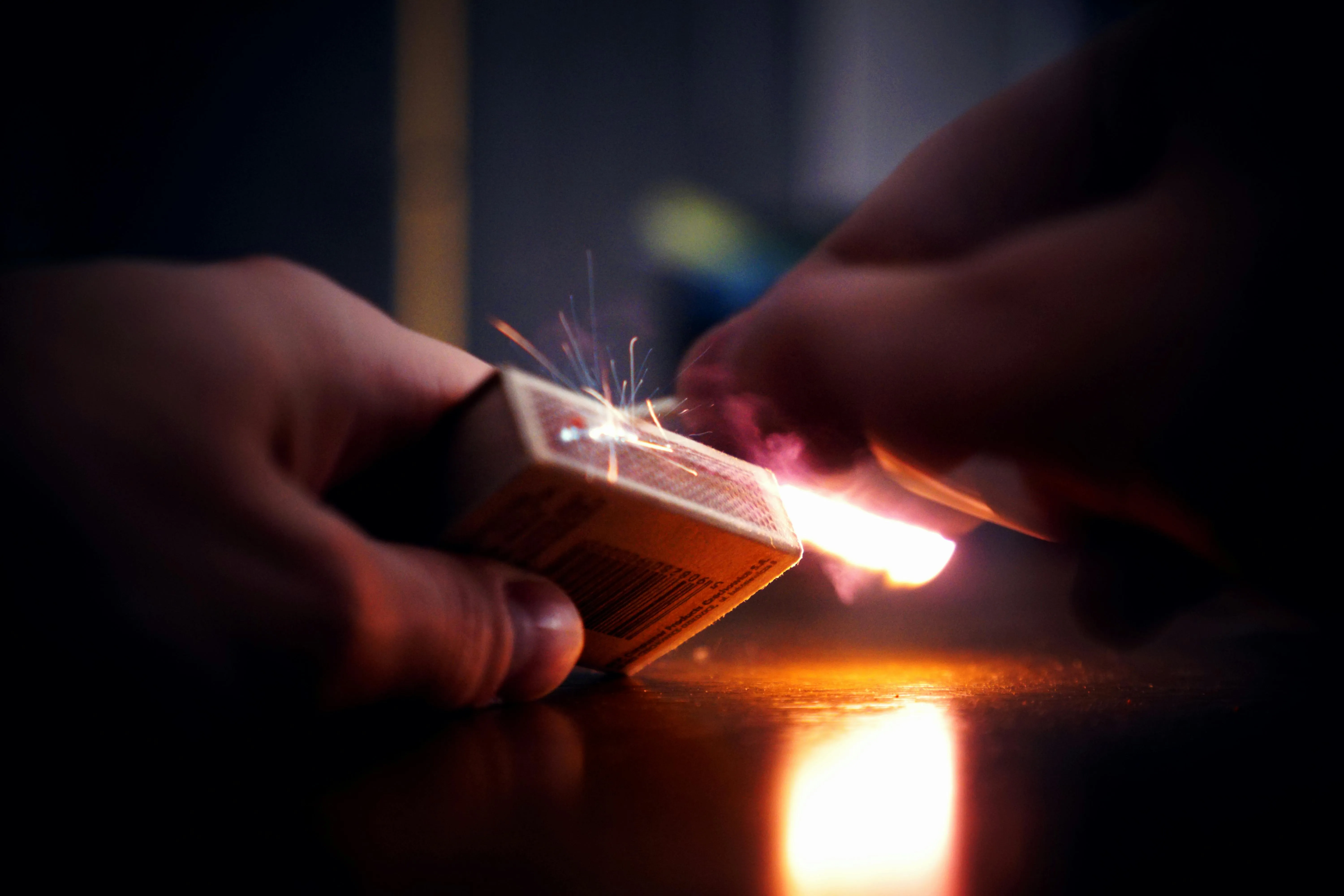 A person lighting a match by rubbing a matchstick against a matchbox's body. 