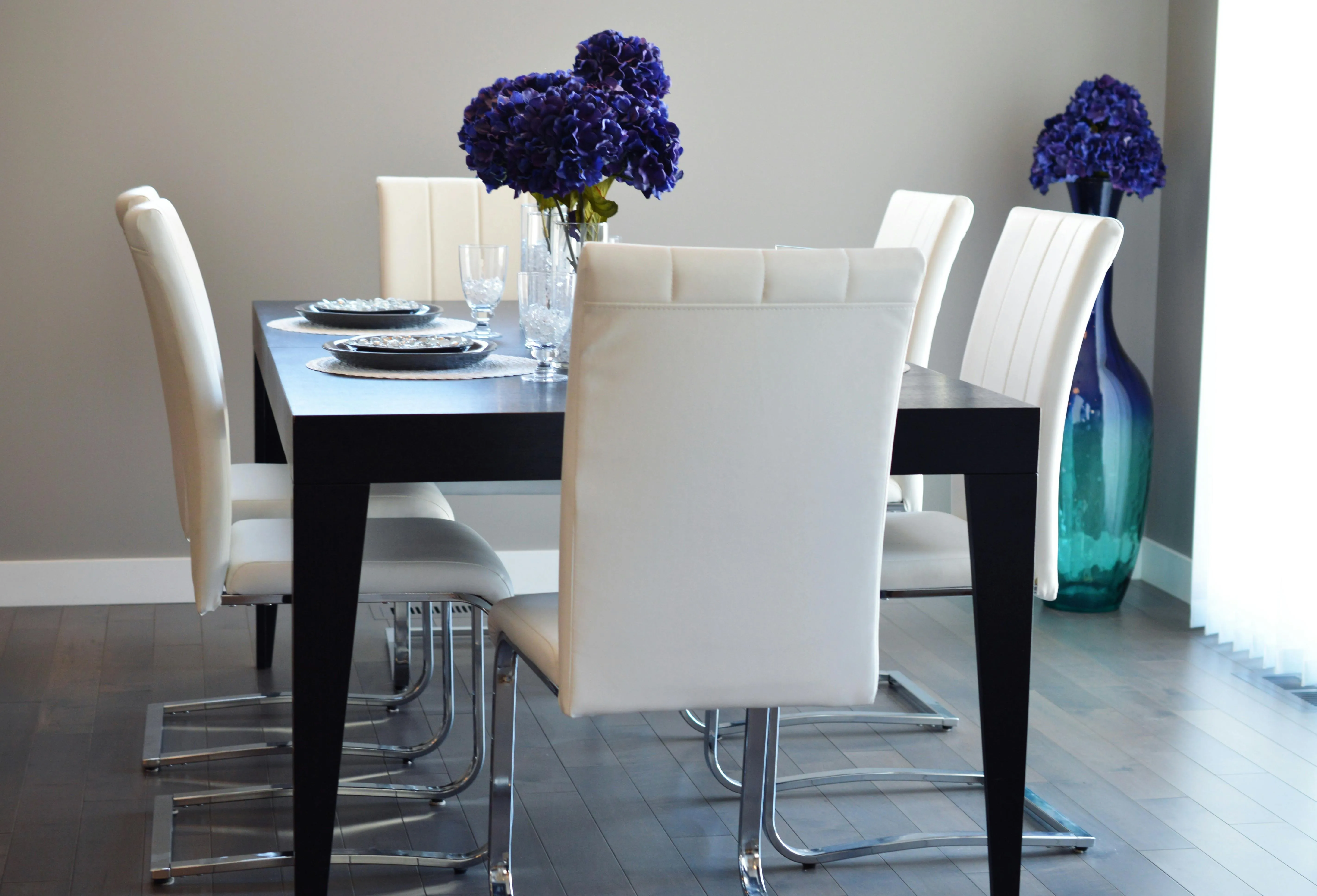 Purple flower on a white wooden dining table along with four chairs of the same color.