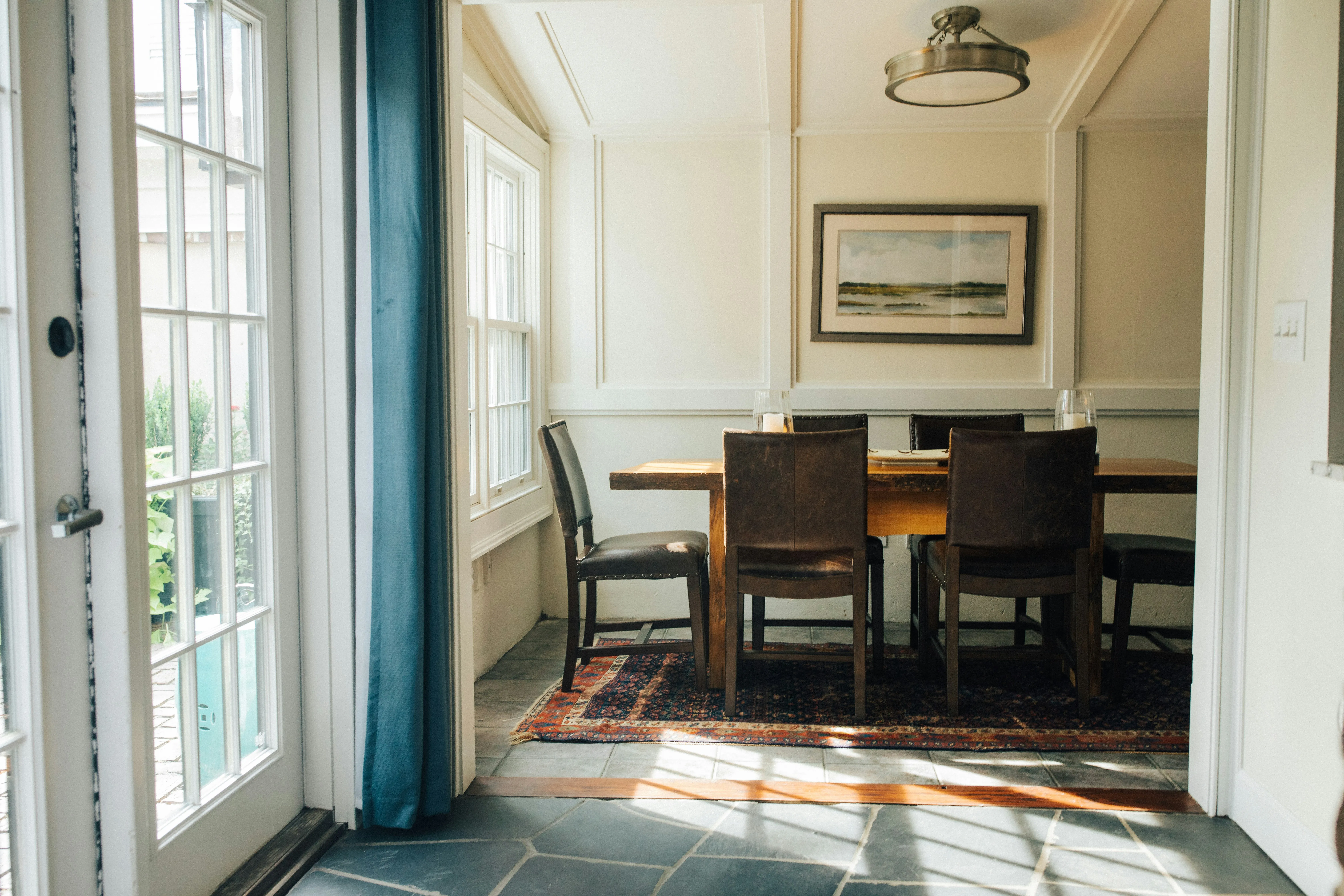 Rectangular wooden dining table with four chairs on a rug in a dining room. On the wall there is  an art piece.