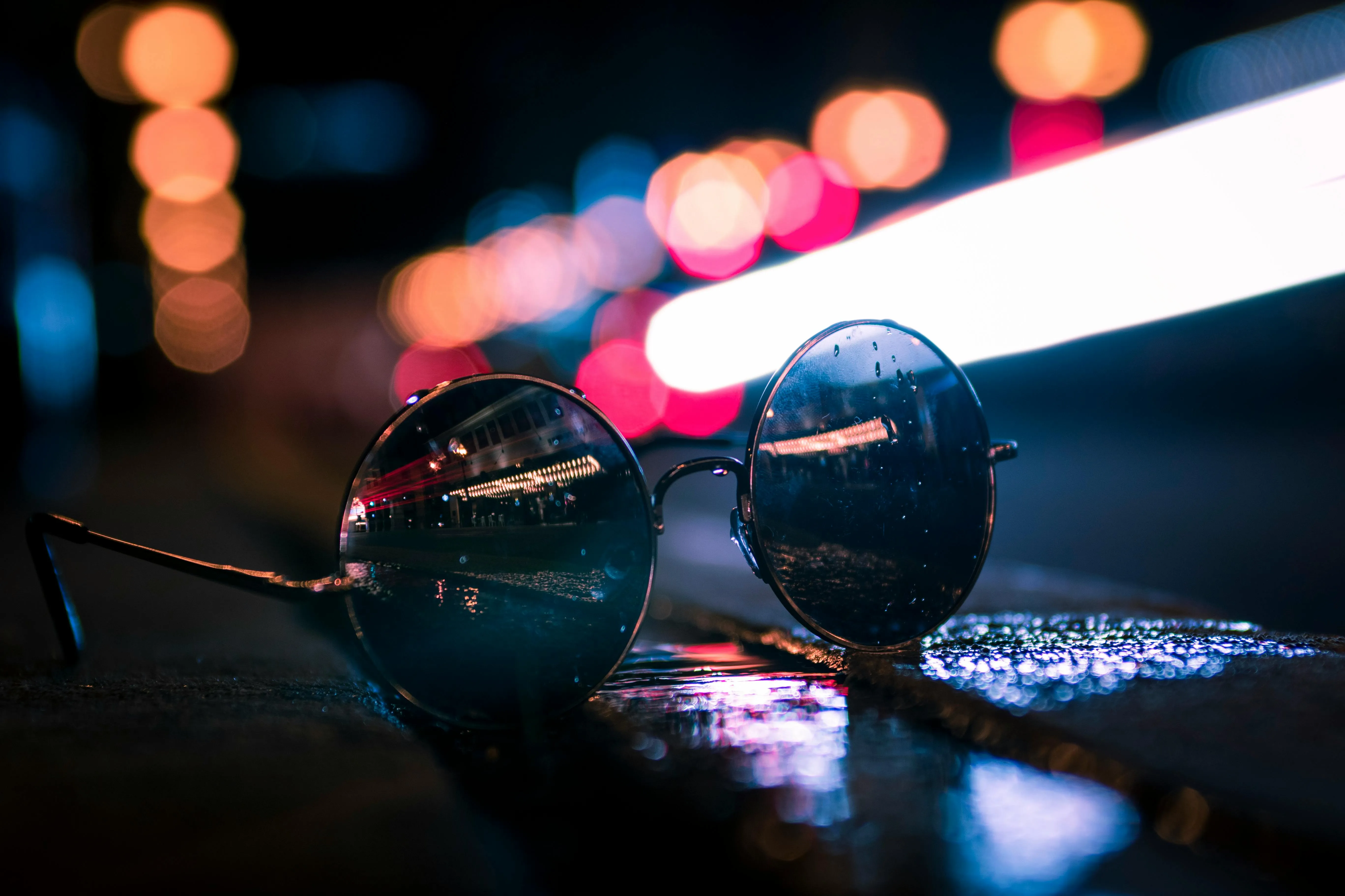 In a nightescape photograph a close-up of a pair of round sunglasses is seen on the ground.