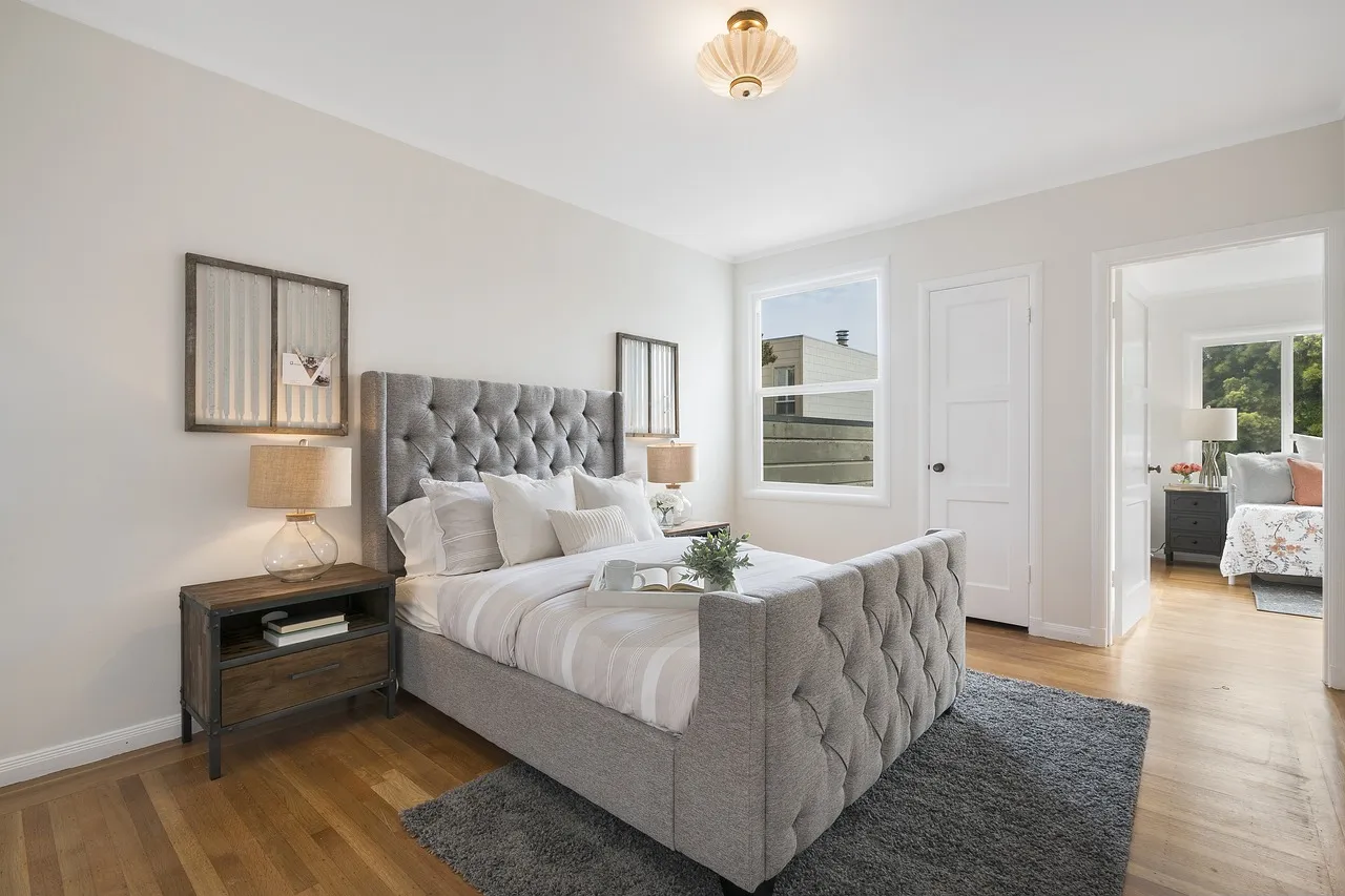 A white bed on a gray rug in a room