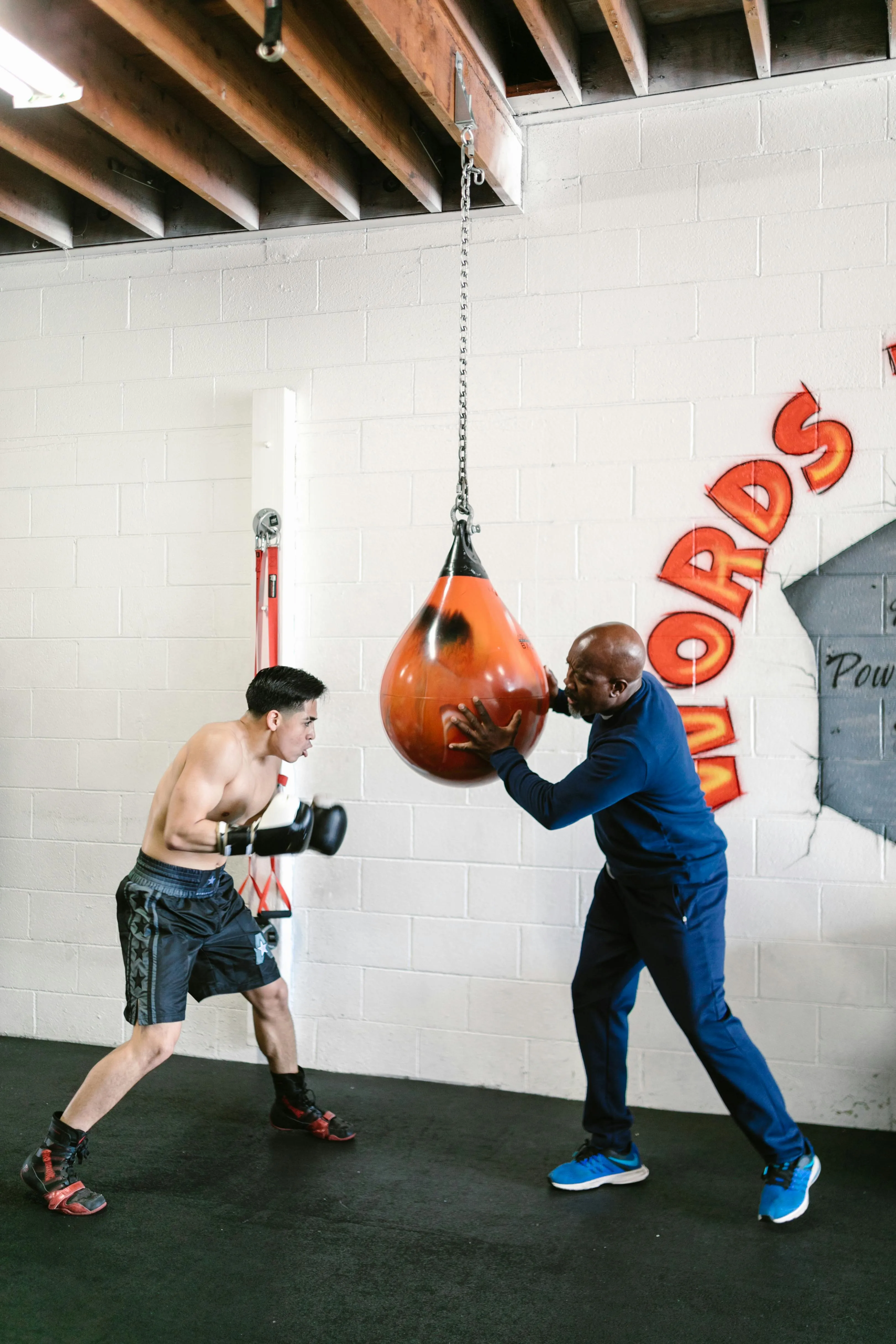 An athlete training on uppercut punching bag in a gym while their coach gives instructions.