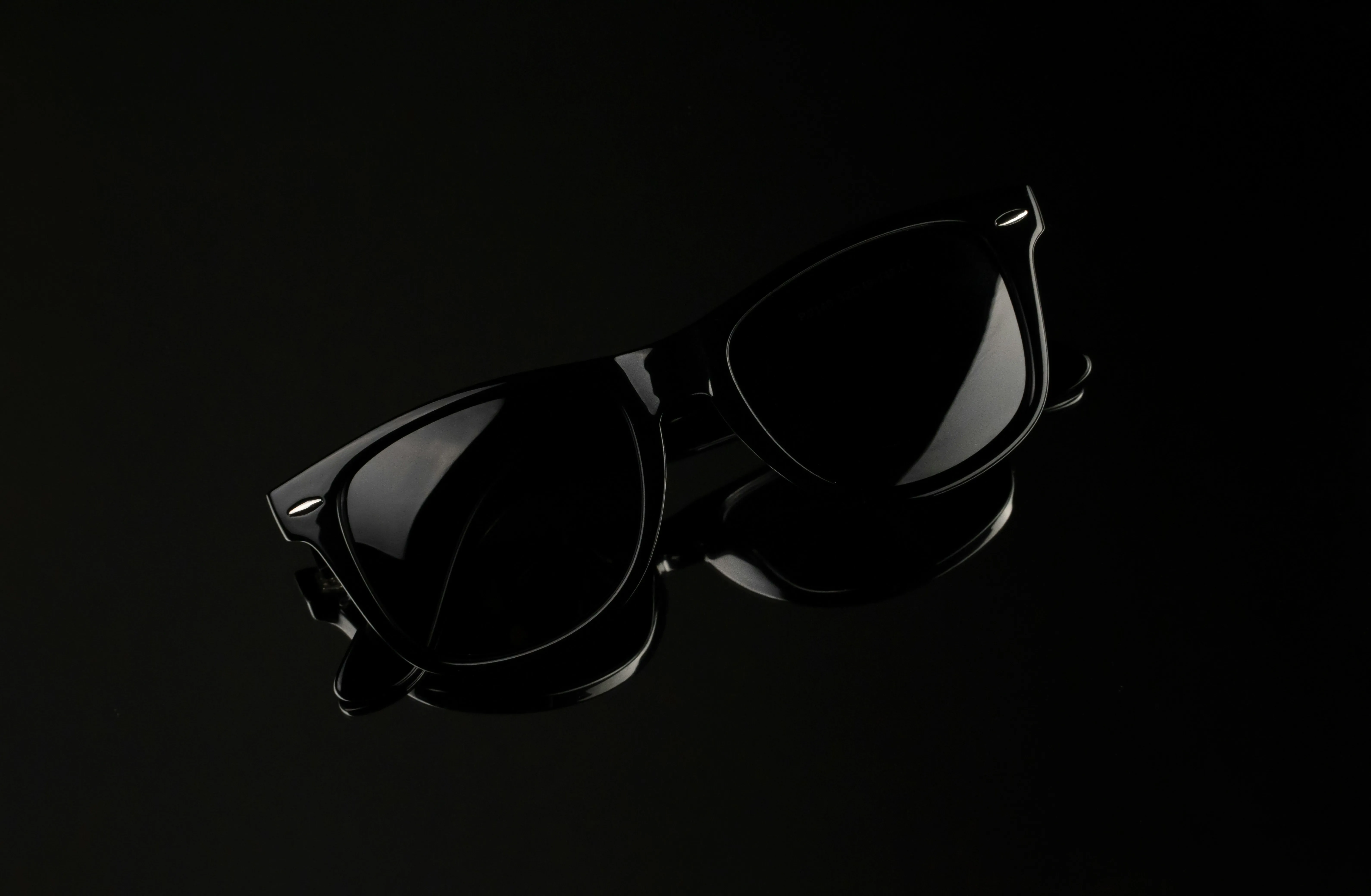 A pair of black wayfarer sunglass on black glossy surface.