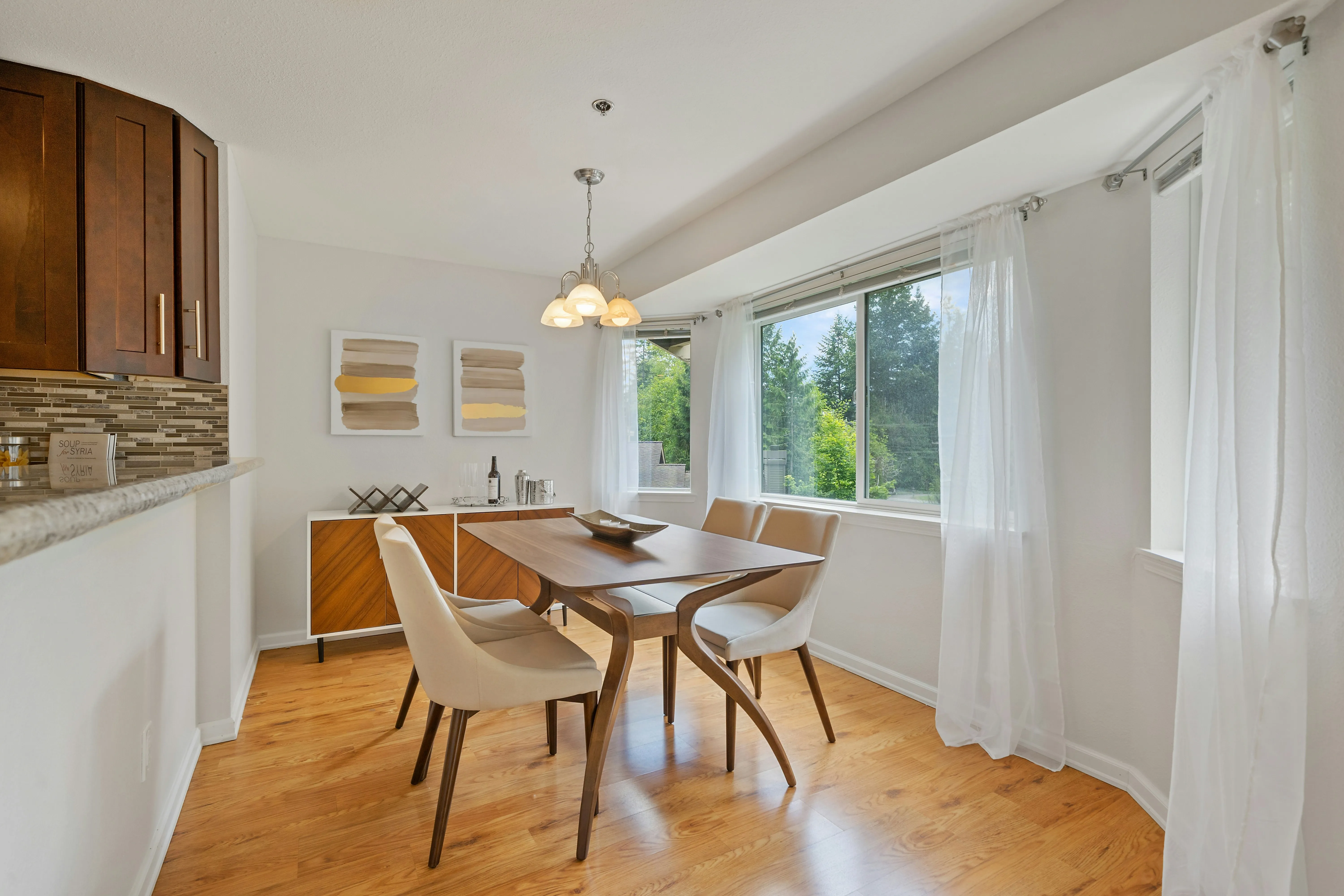 Beige wooden table with wooden chairs near window. There's hanging light there.