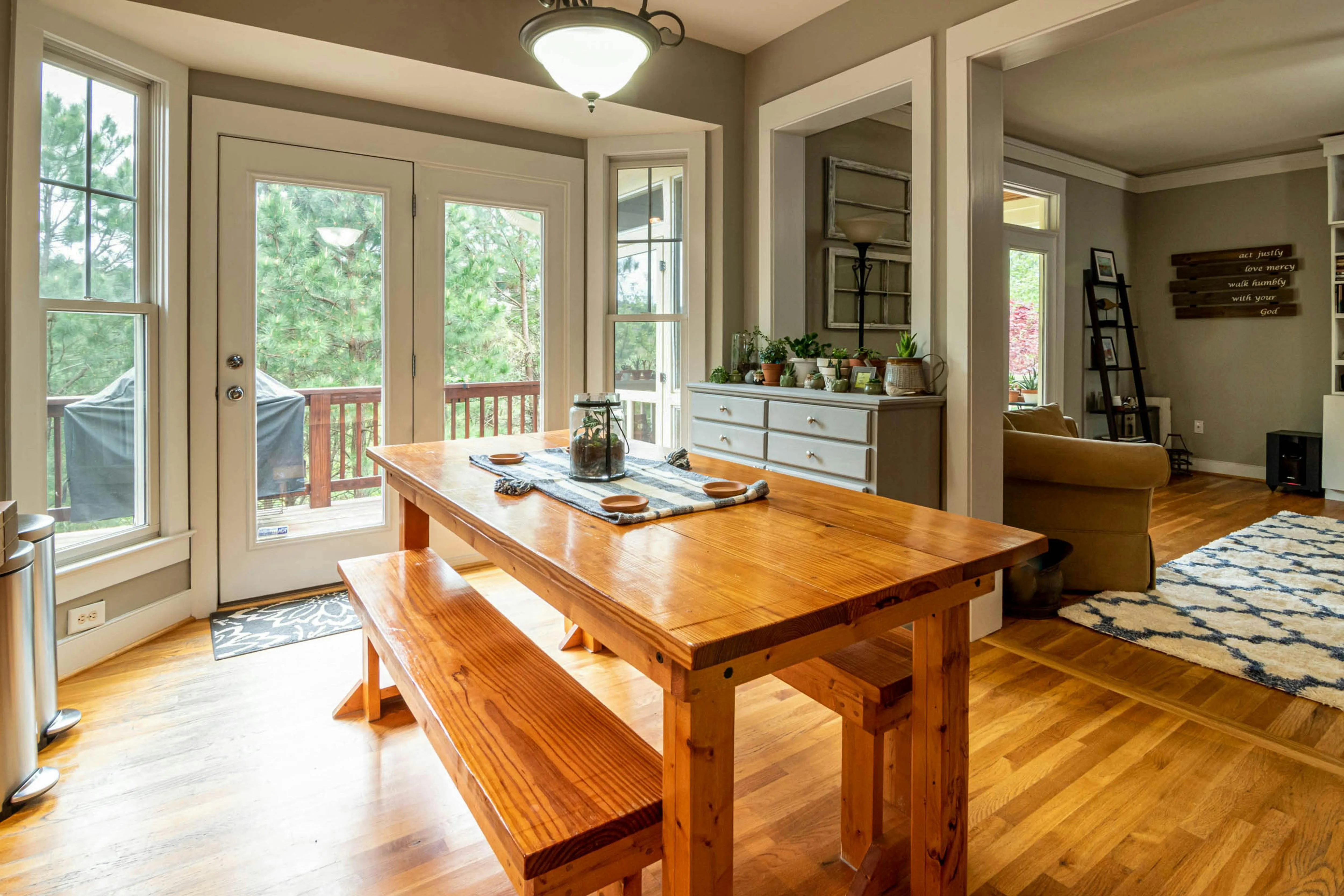 A wooden dining table along with a wooden bench in a dining room with big windows and doors.