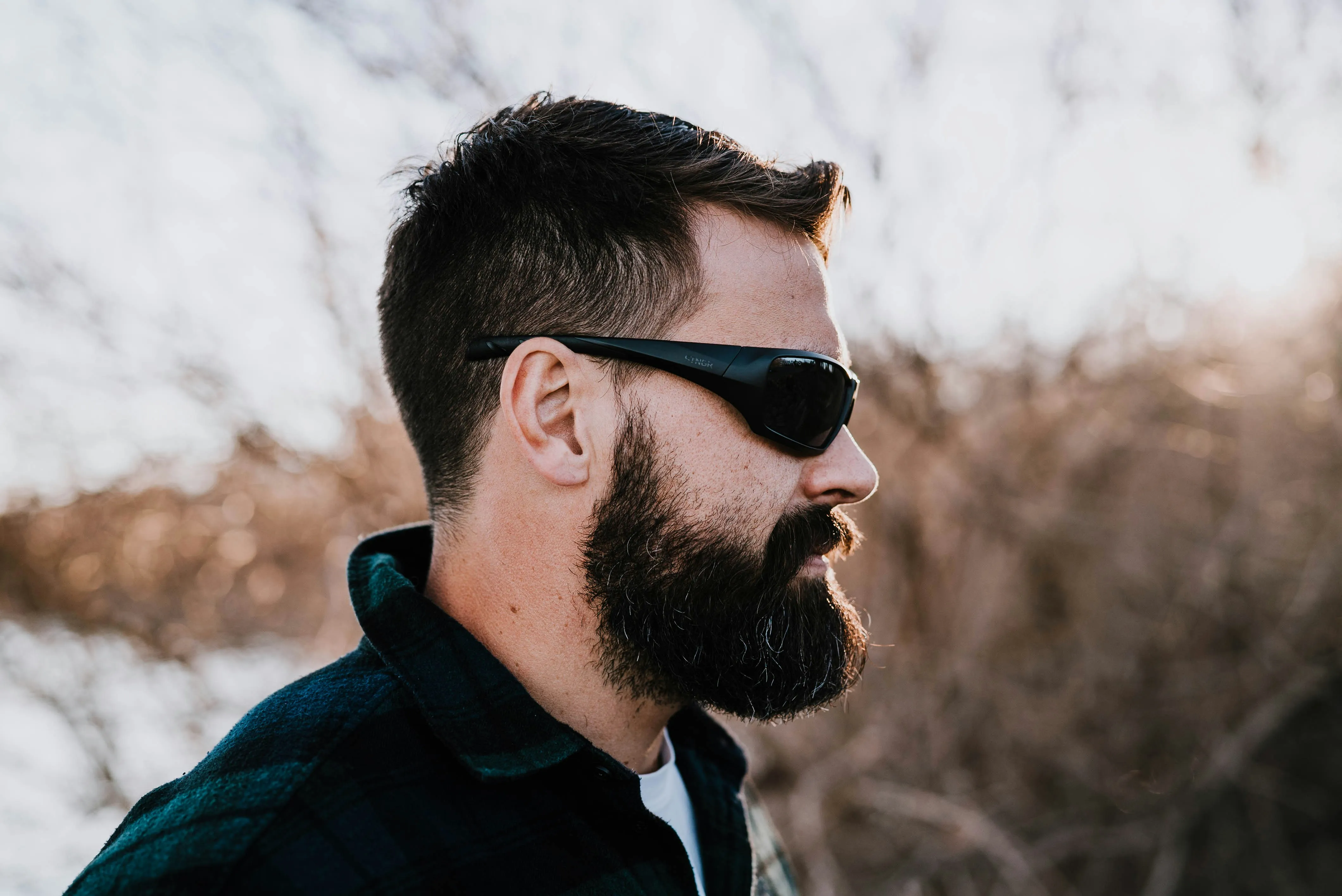 A person with black and green color jacket wearing a pair of black wraparound sunglasses.