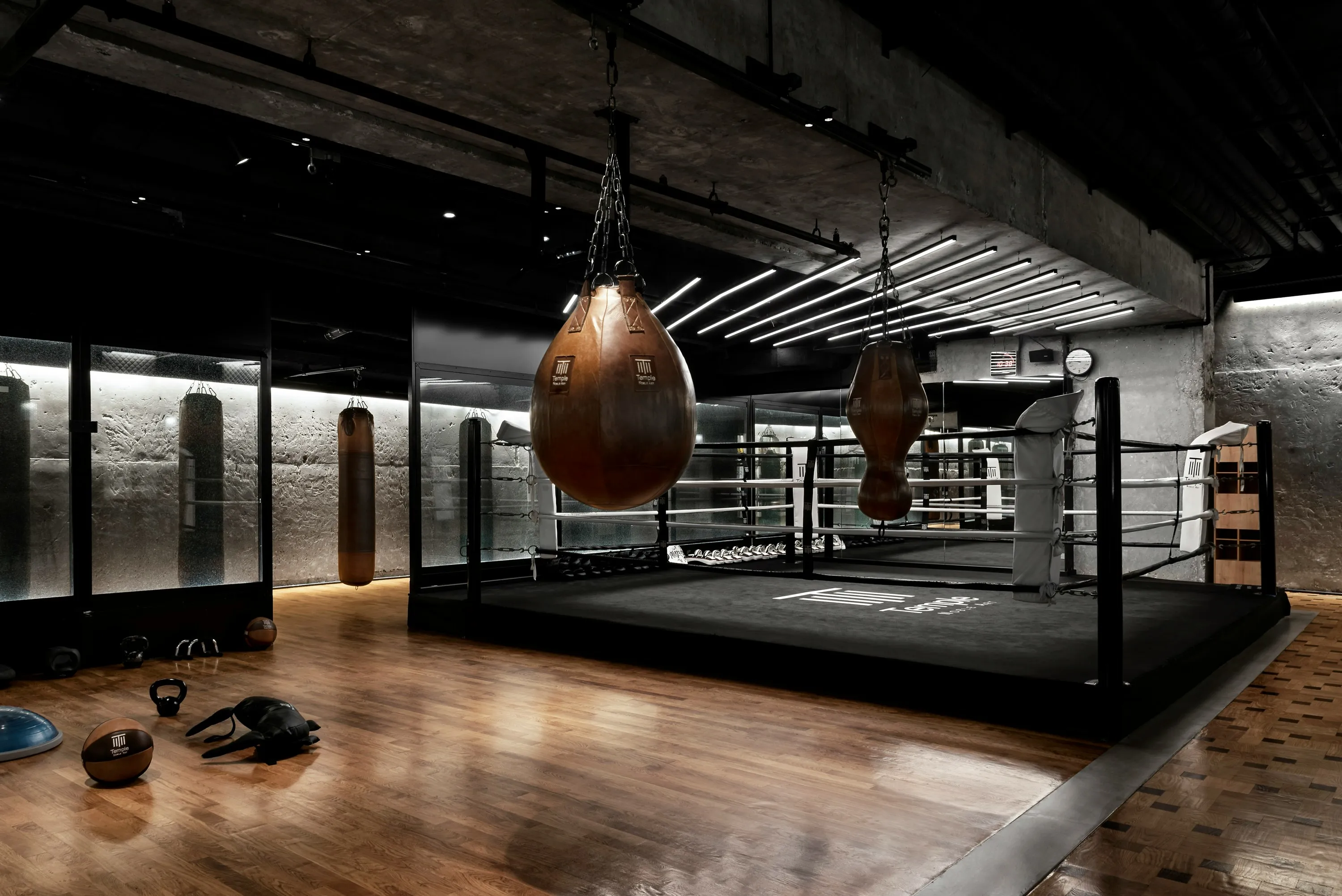 A brown colored wrecking heavy punching bag hung from the ceiling in a gym with other bags in the background.