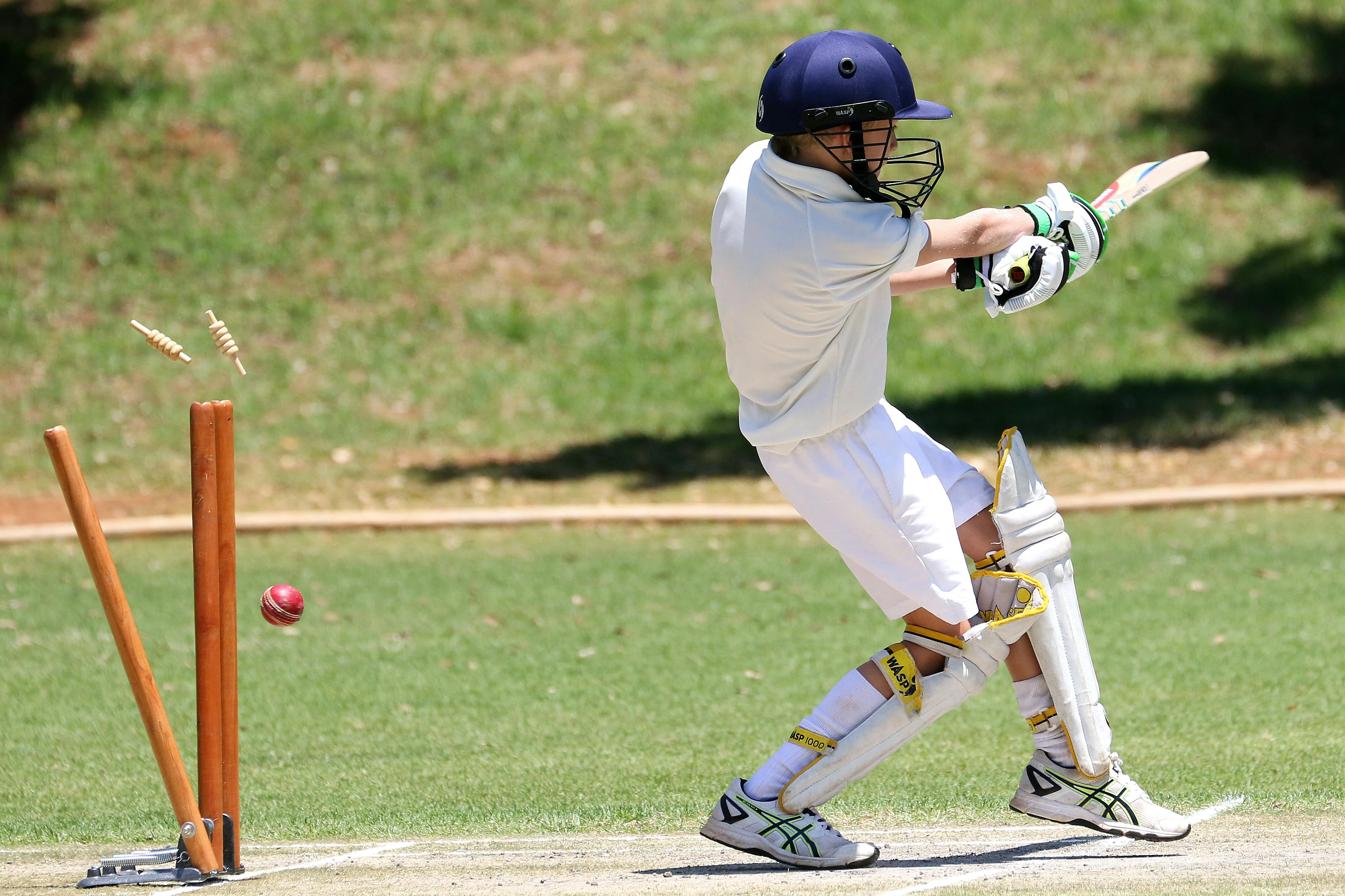 A boy playing cricket while his wicket falls as the ball hits the stumps and dislodged the bails.webp