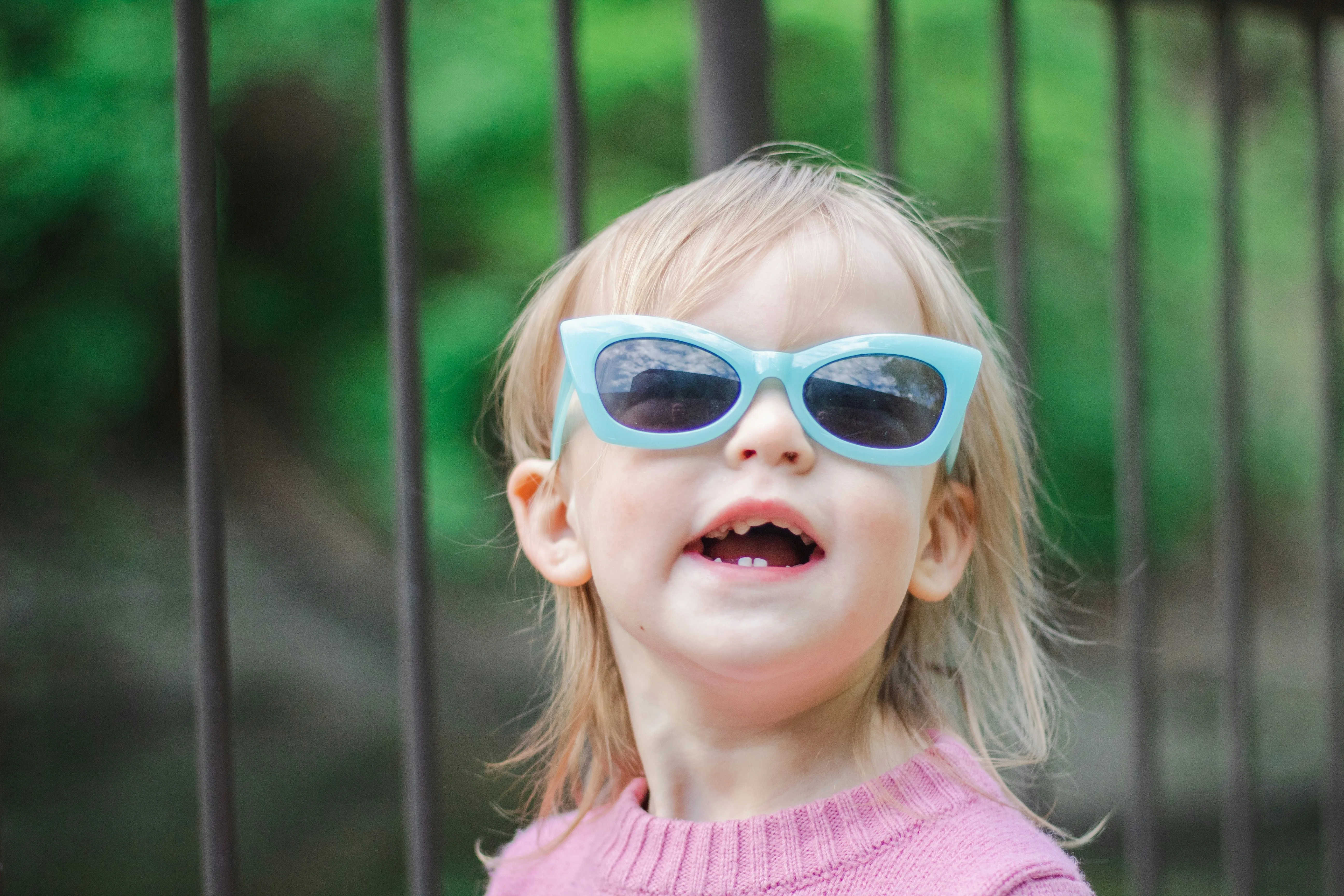 A litle girl wearing a pair of turquoise colored cat-eye sunglass.