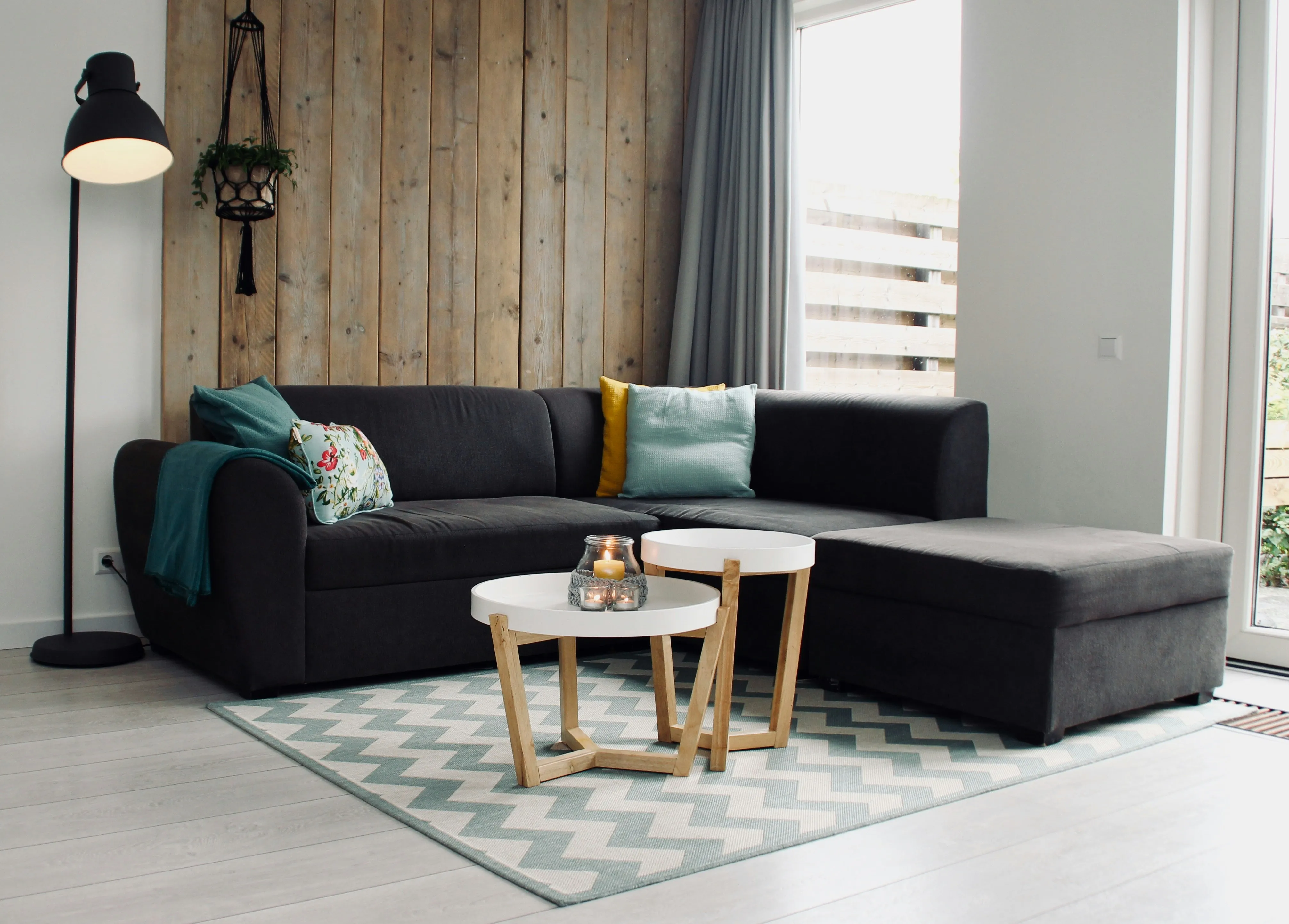 A light green and white rug with a zigzag design is placed in a modern room. There are two sofas and two little tables on the rug. The room also has a lamp and a hanged plant.