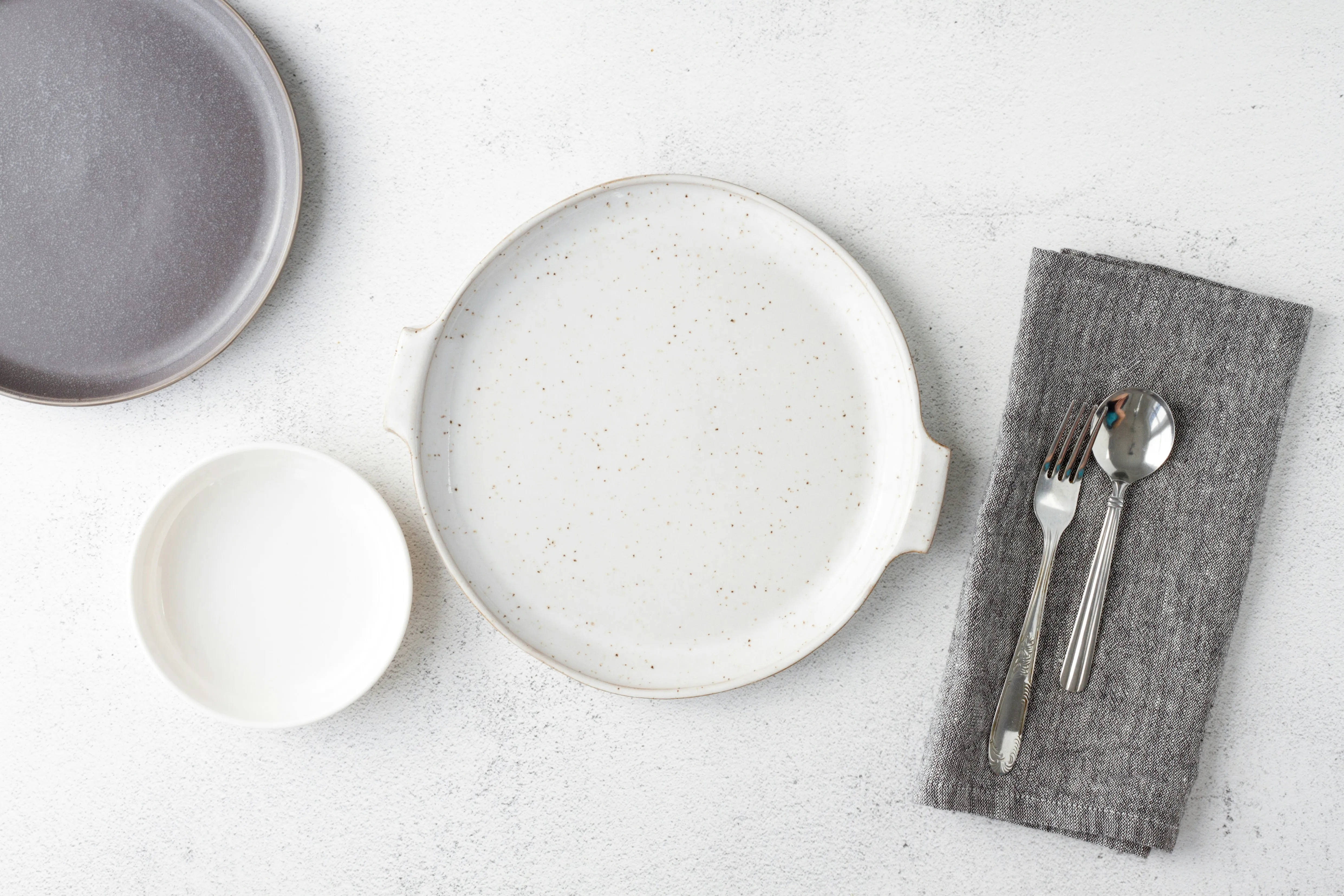 A table set with plates and cutlery, with the silver cutlery sitting on greyish handkerchief used as napkin.