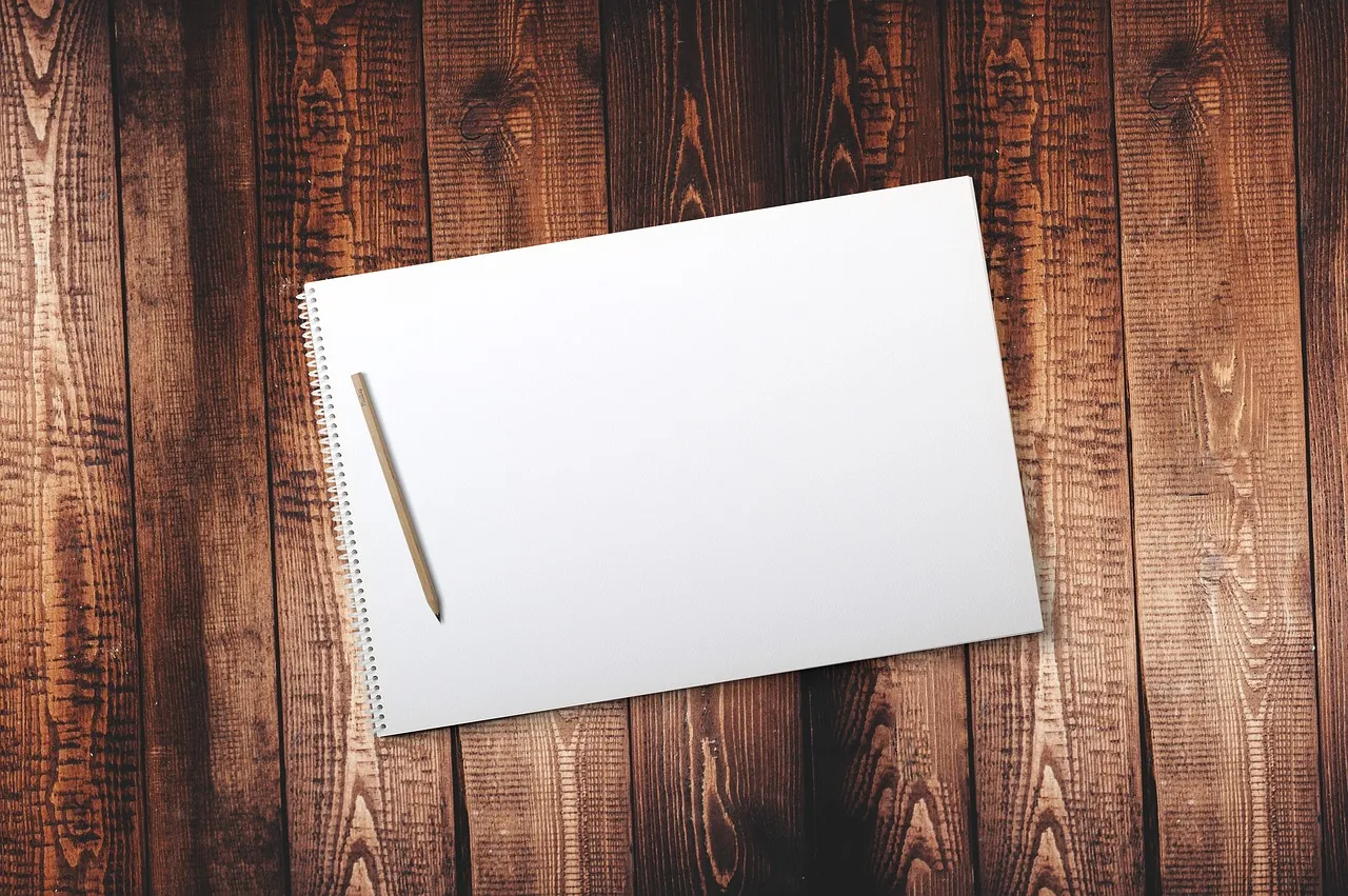  A note pad on a wooden surface with a pencil on it.