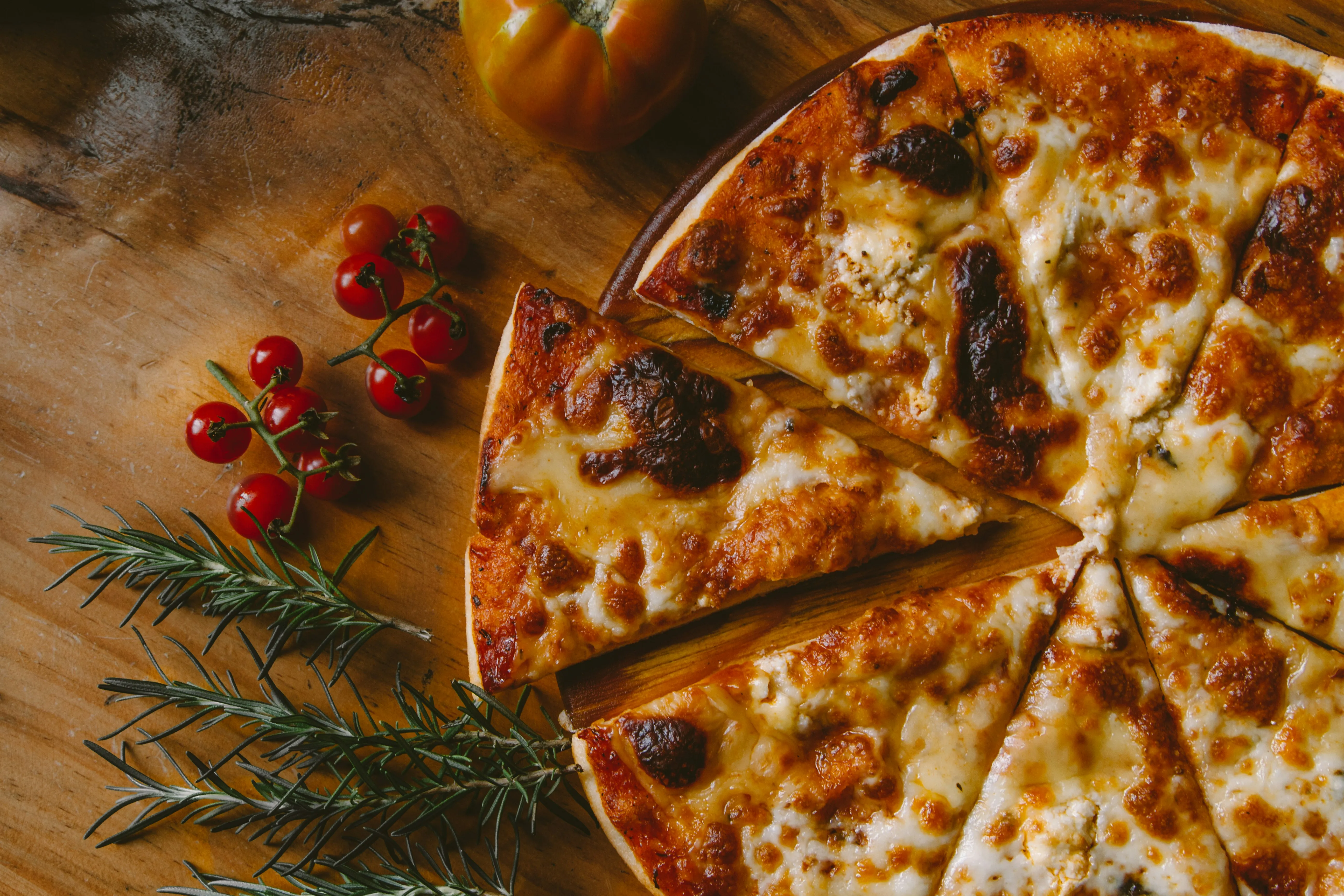 A freshly baked and cut pizza on a wooden surface along with some berries and spruce leaves