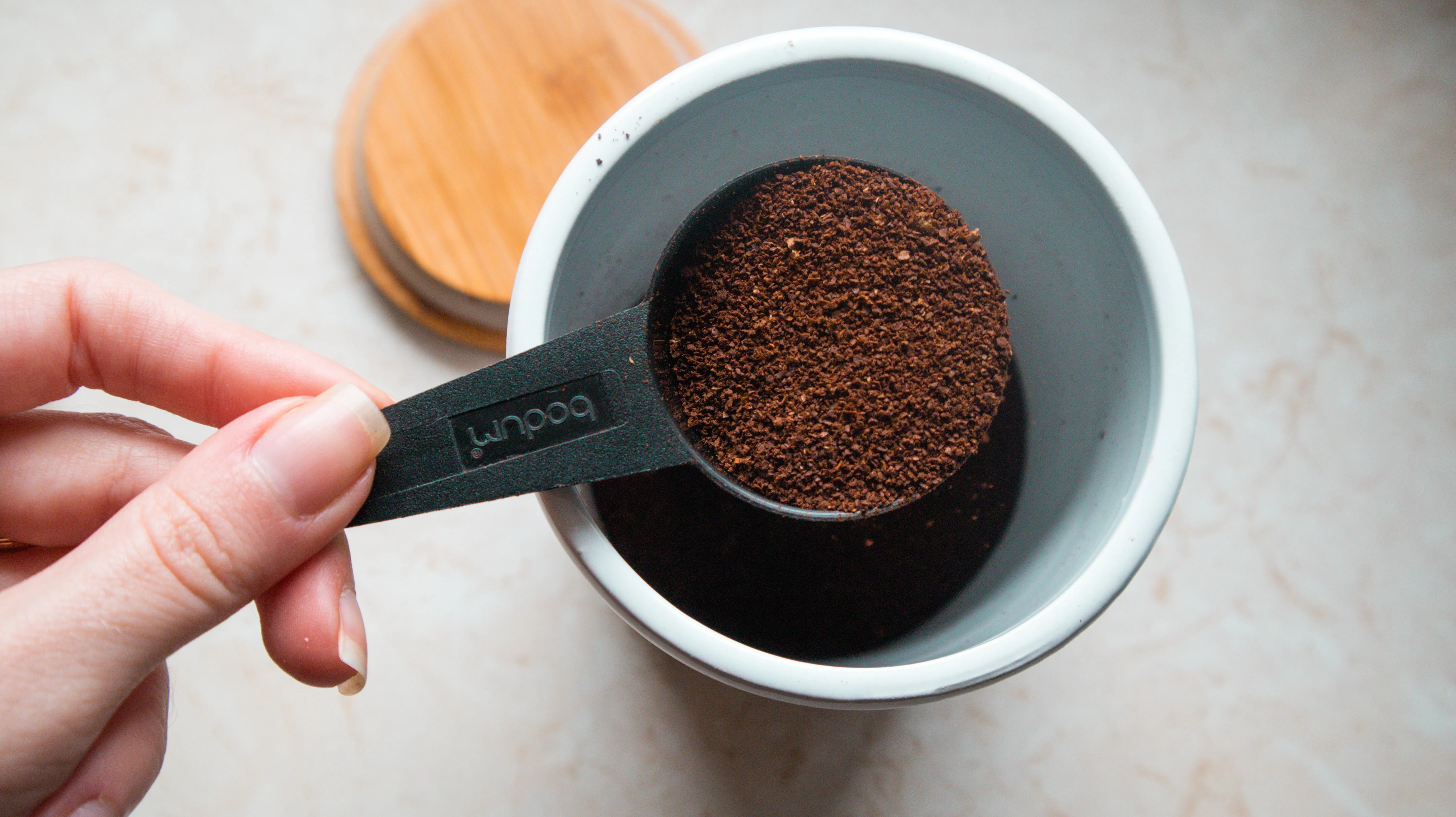 A scoop of coffee taken out from a ground coffee holder. Its lid is rested on the platform beside the jar.